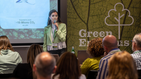 Frau im gr&uuml;nen Blazer mit Mikrophon spricht zu Teilnehmenden
