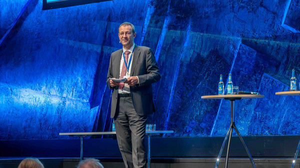  Mann h&auml;lt auf der B&uuml;hne einen Vortrag, im Hintergrund Chard mit der Aufschrift "Bildung f&uuml;r ein starkes Europa: Berthold H&uuml;bers, Leiter der Nationalen Agentur"