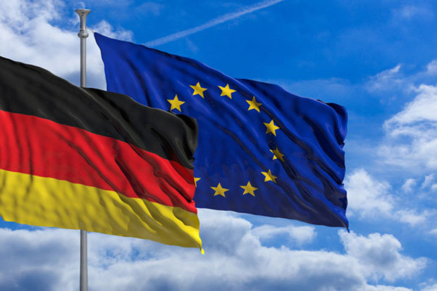 Deutsche und europ&auml;ische Flagge wehen im Wind vor einem blauen Himmel mit Wolken. 
