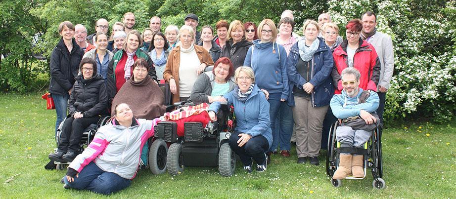 Eine größere Gruppe von Personen. Einige stehen, andere sitzen im Rollstuhl.