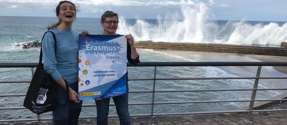 Zwei Frauen halten ein Tuch am Meer stehend hoch