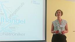 Foto: Anika Roshan steht rechts neben der Leinwand auf der ihre Präsentation zu sehen ist und spricht