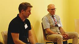 Fotos: zwei Personen sitzen nebeneinander auf Stühlen und hören der Diskussion zu