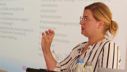 Foto: Julia Lubjuhn spricht und gestikuliert mit der Hand, im Hintergrund sieht man die Präsentation