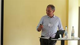 Foto: Stefan Metzdorf lehnt an einem Stehtisch und ist zur Leinwand mit der Präsentation gerichtet